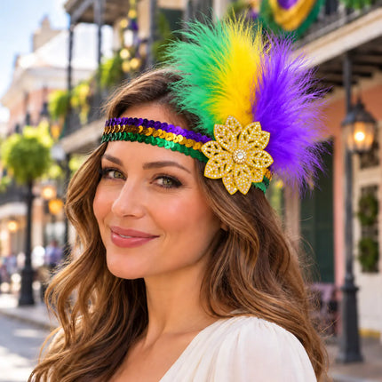 A woman wearing a festive Mardi Gras feathered headband with green, yellow, and purple feathers, purple and gold sequins, and a gold flower embellishment, set against a blurred street background.