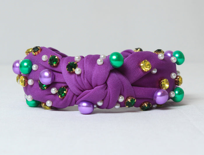 Close-up side view of a woman wearing a purple Mardi Gras knotted headband embellished with pearls, rhinestones, and colorful bead